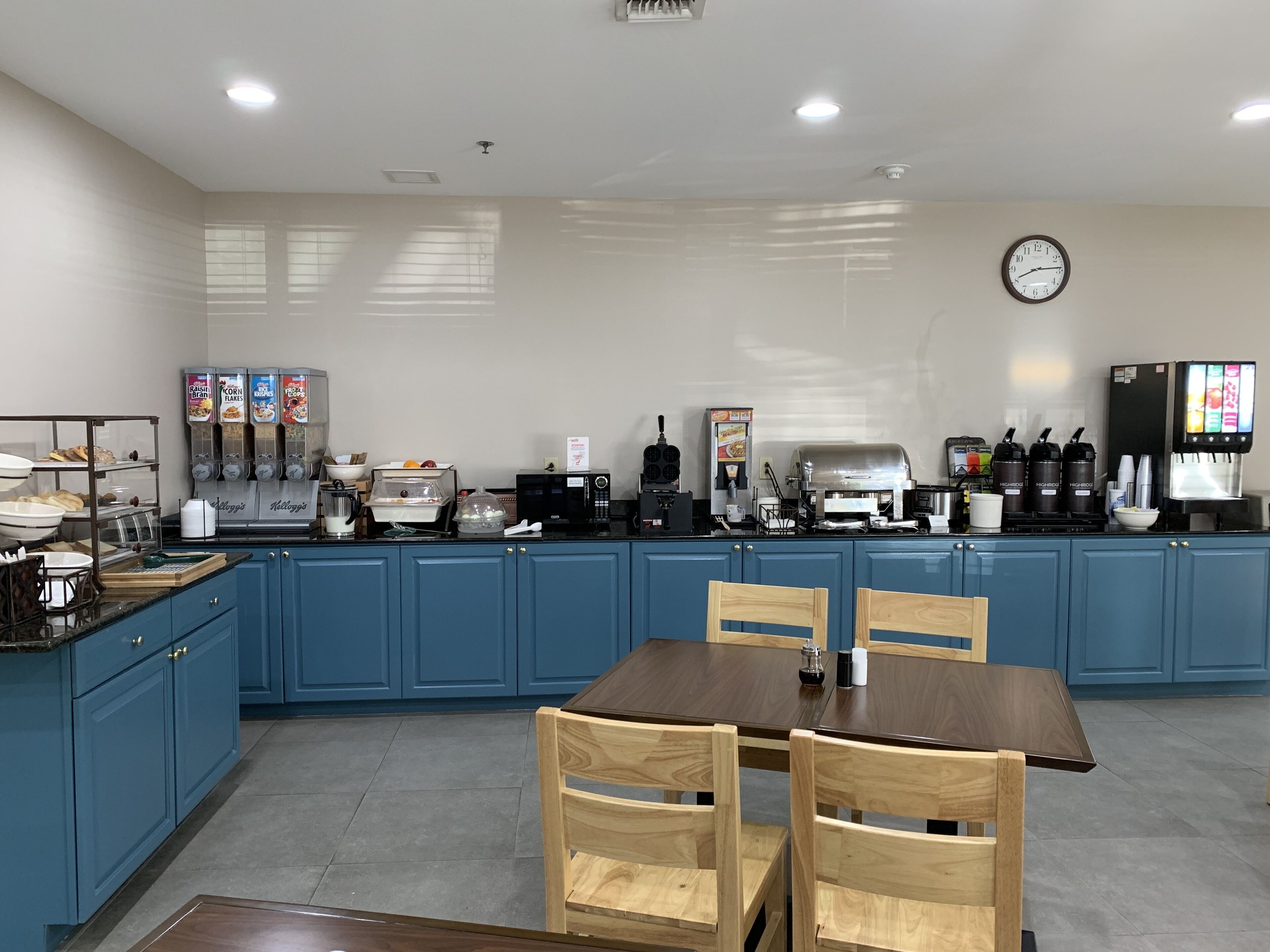 A kitchen with blue cabinets, a wooden table, and various appliances including a coffee machine and a microwave.