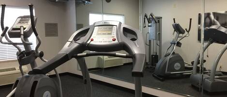 Et fitnessrum med løbebånd, spinningcykler og et spejl.