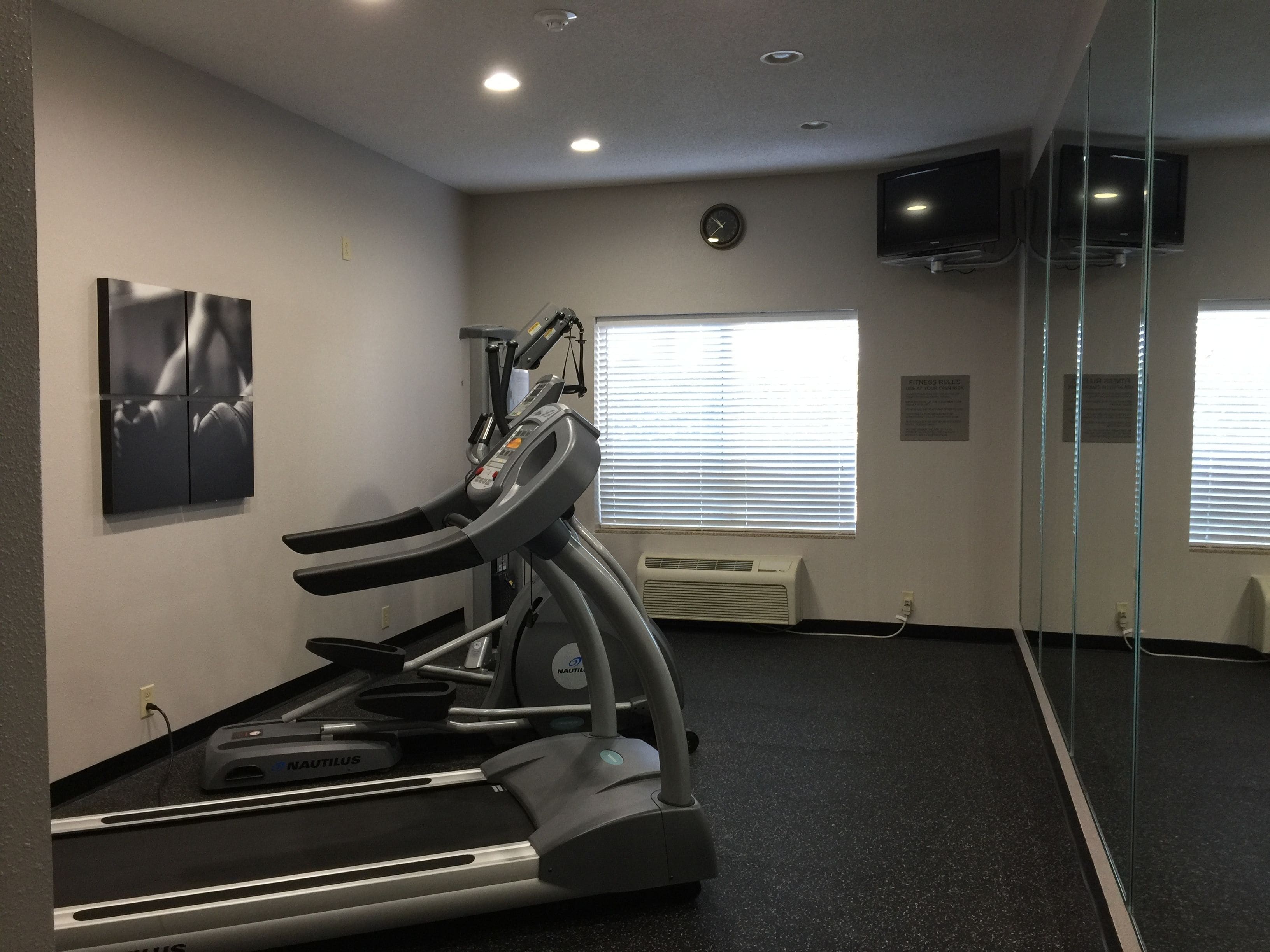 A gym with treadmills, a wall-mounted clock, and a TV on the wall.