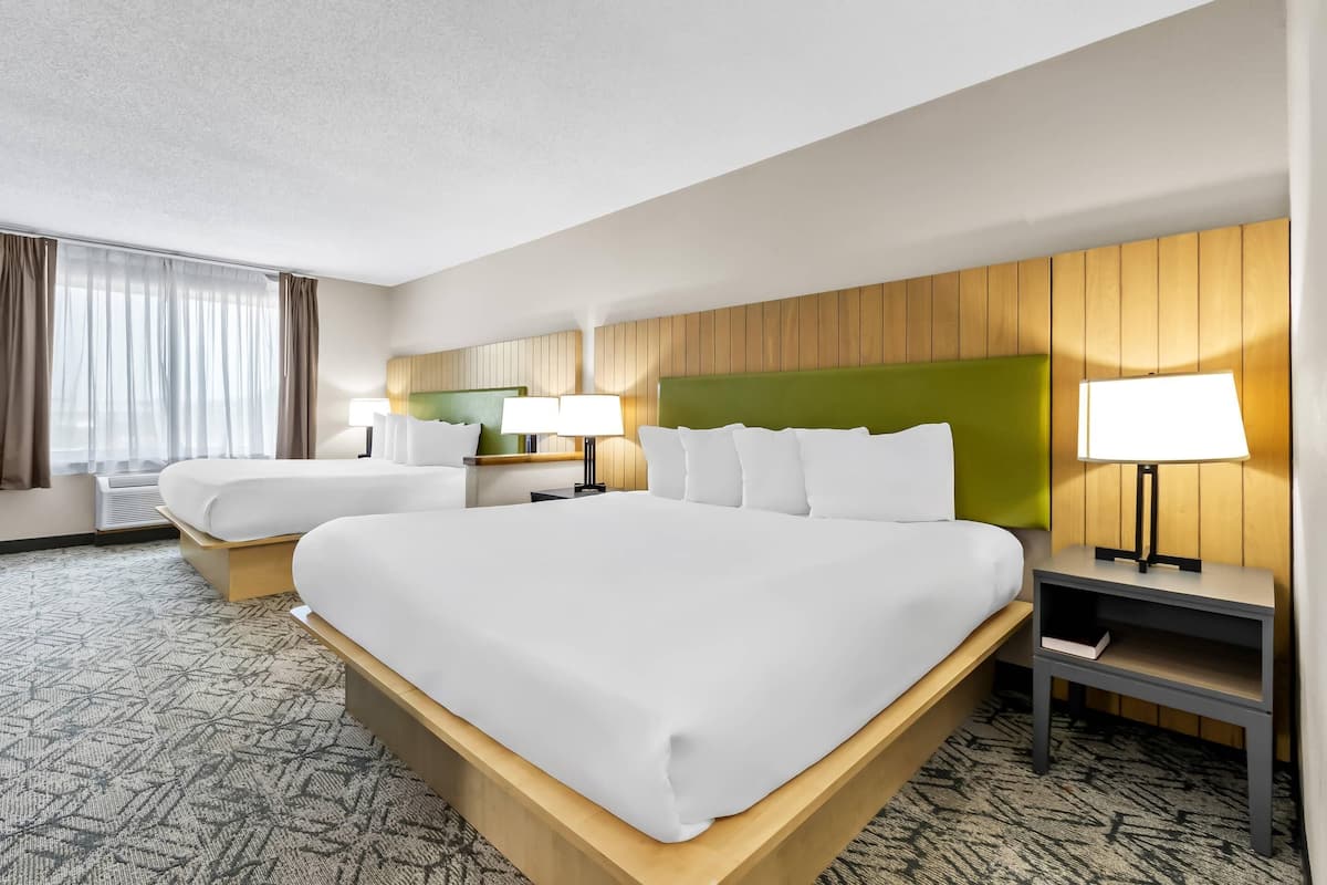 A hotel room with two beds, a wooden headboard, a nightstand with a lamp, and a patterned carpet.