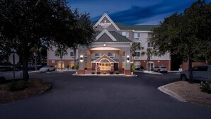 Un Hotel Country Inn & Suites amb entrada central, envoltat d'aparcament i arbres.
