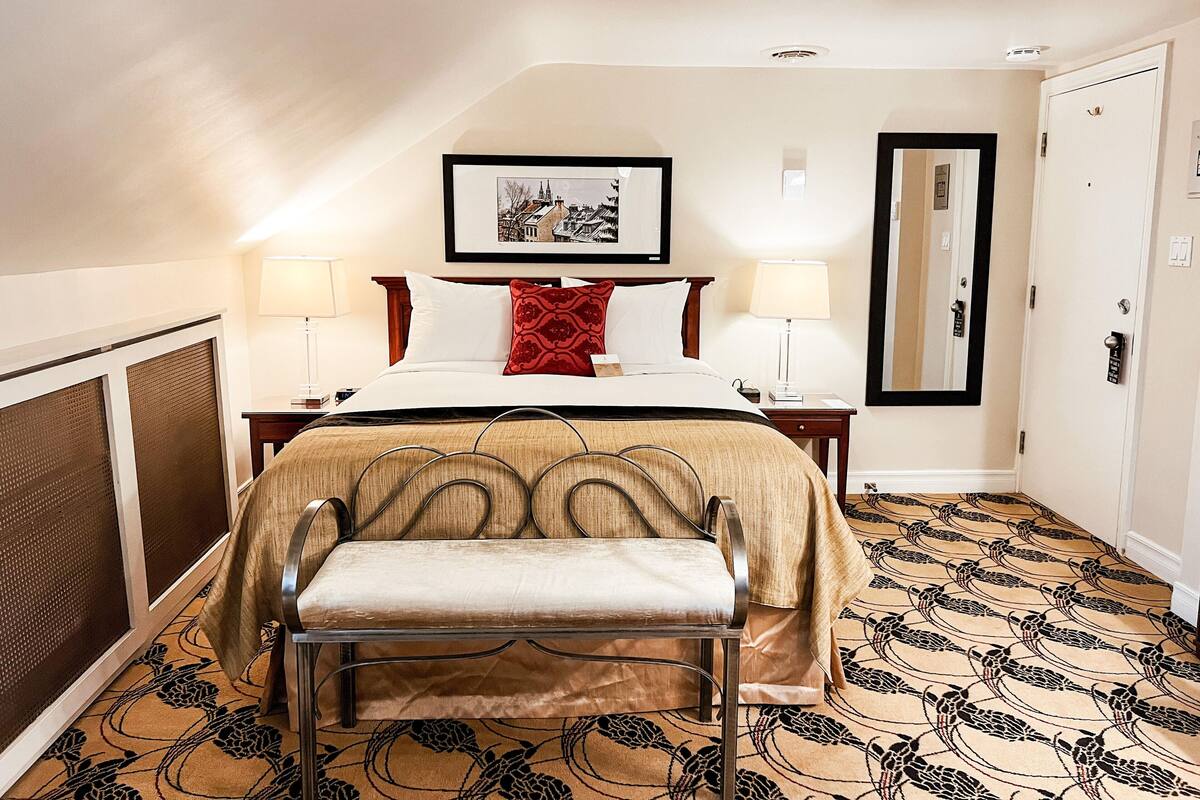 A hotel room with a bed, two bedside lamps, a large mirror, a chair, and a patterned carpet.