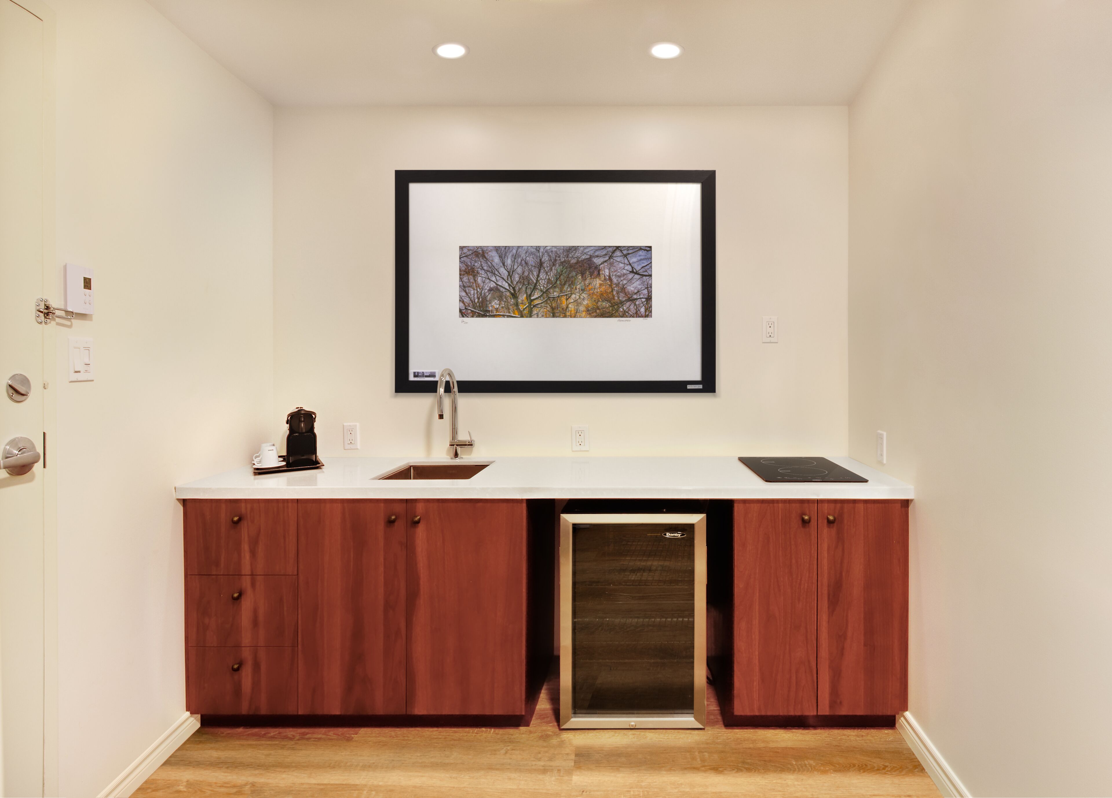 A modern kitchen with a built-in dishwasher, wooden cabinets, a white countertop, and a framed picture above the sink.