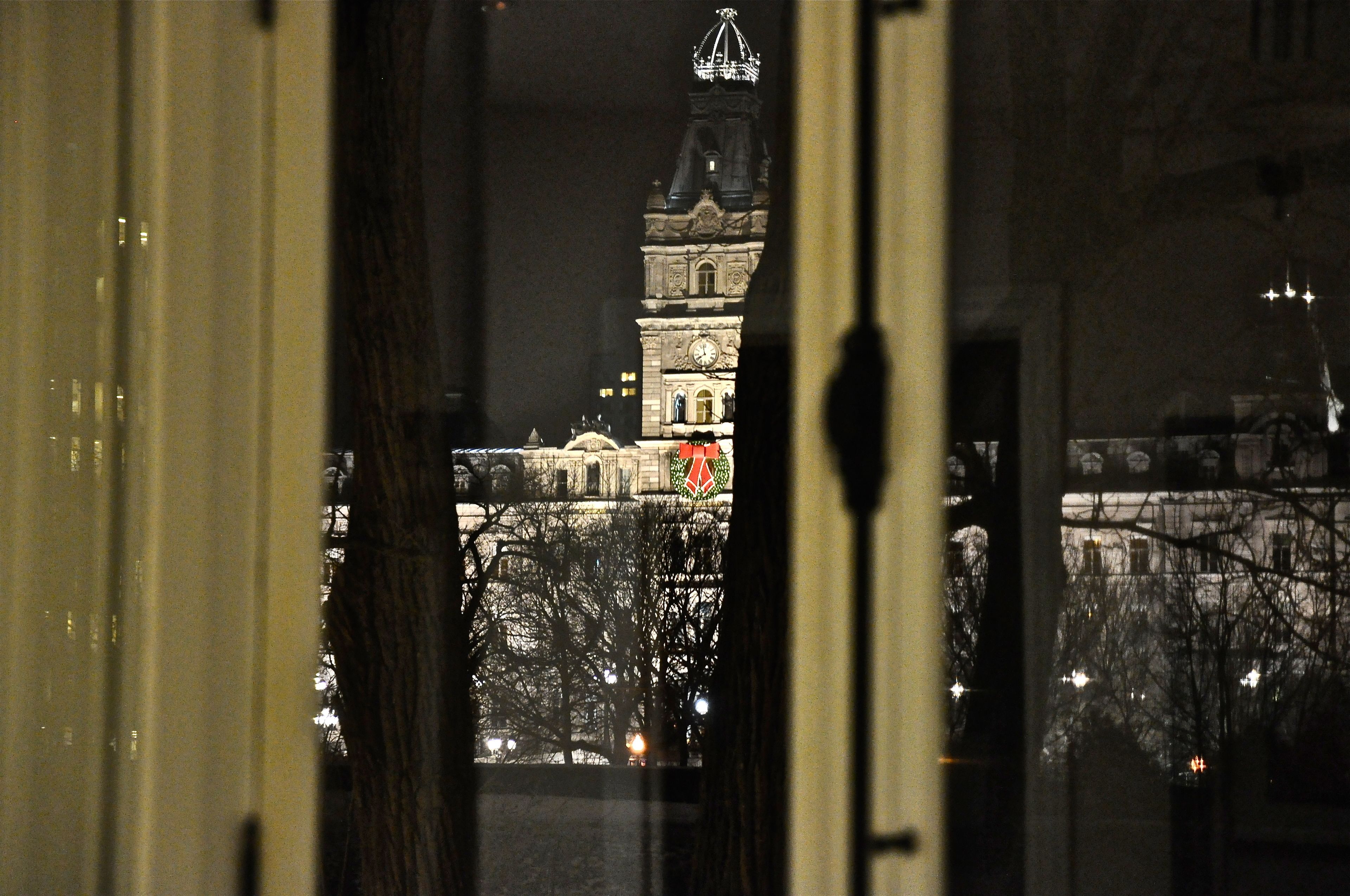 Vista de um edifício histórico com torre de relógio, vista através de uma janela com cortina visível.