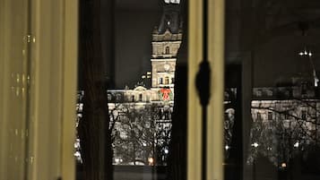Vista de um edifício histórico com torre de relógio, vista através de uma janela com cortina visível.