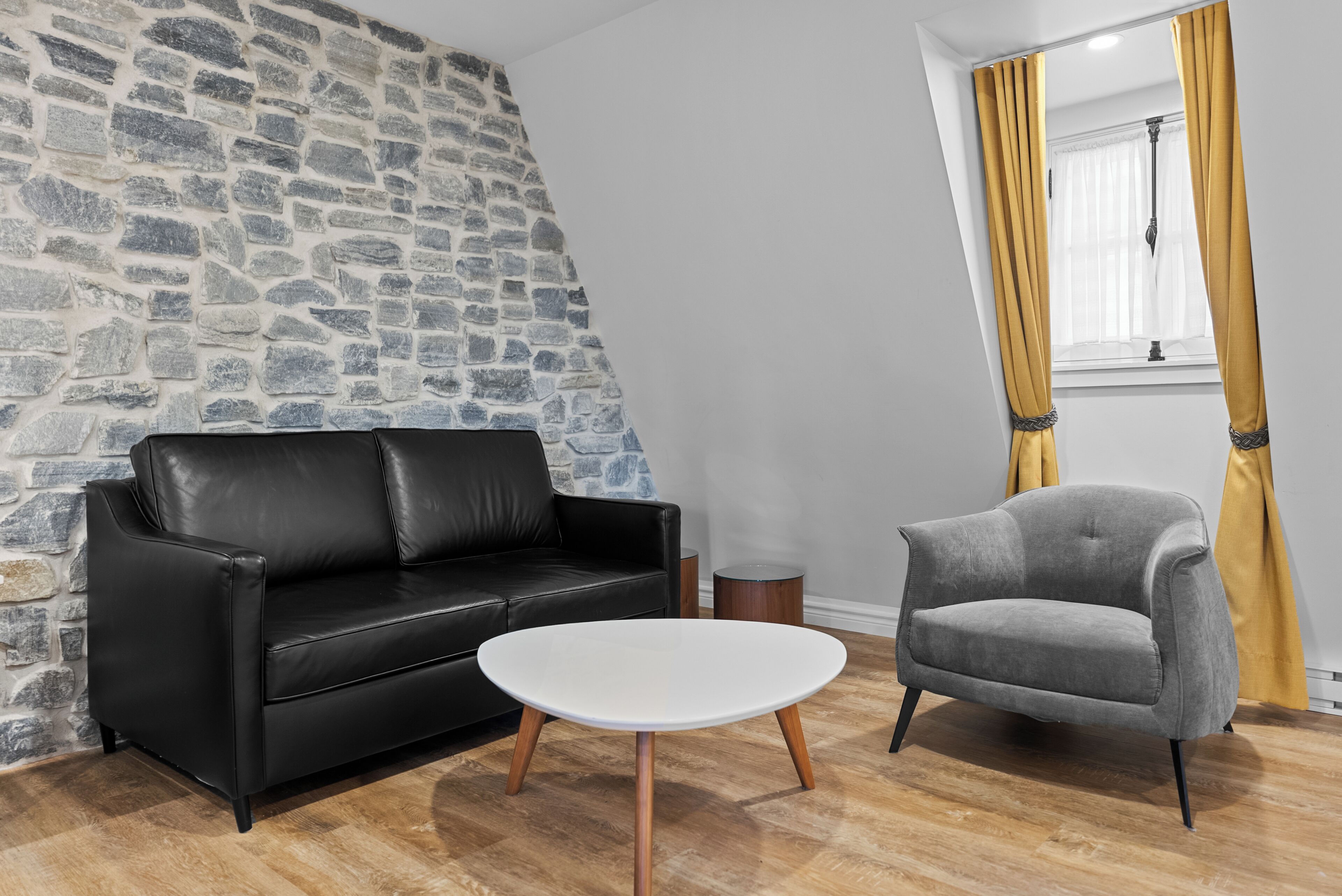 Una habitació amb una paret de pedra, un sofà de cuir negre, un armari de seients gris i una taula de cafè blanca.
