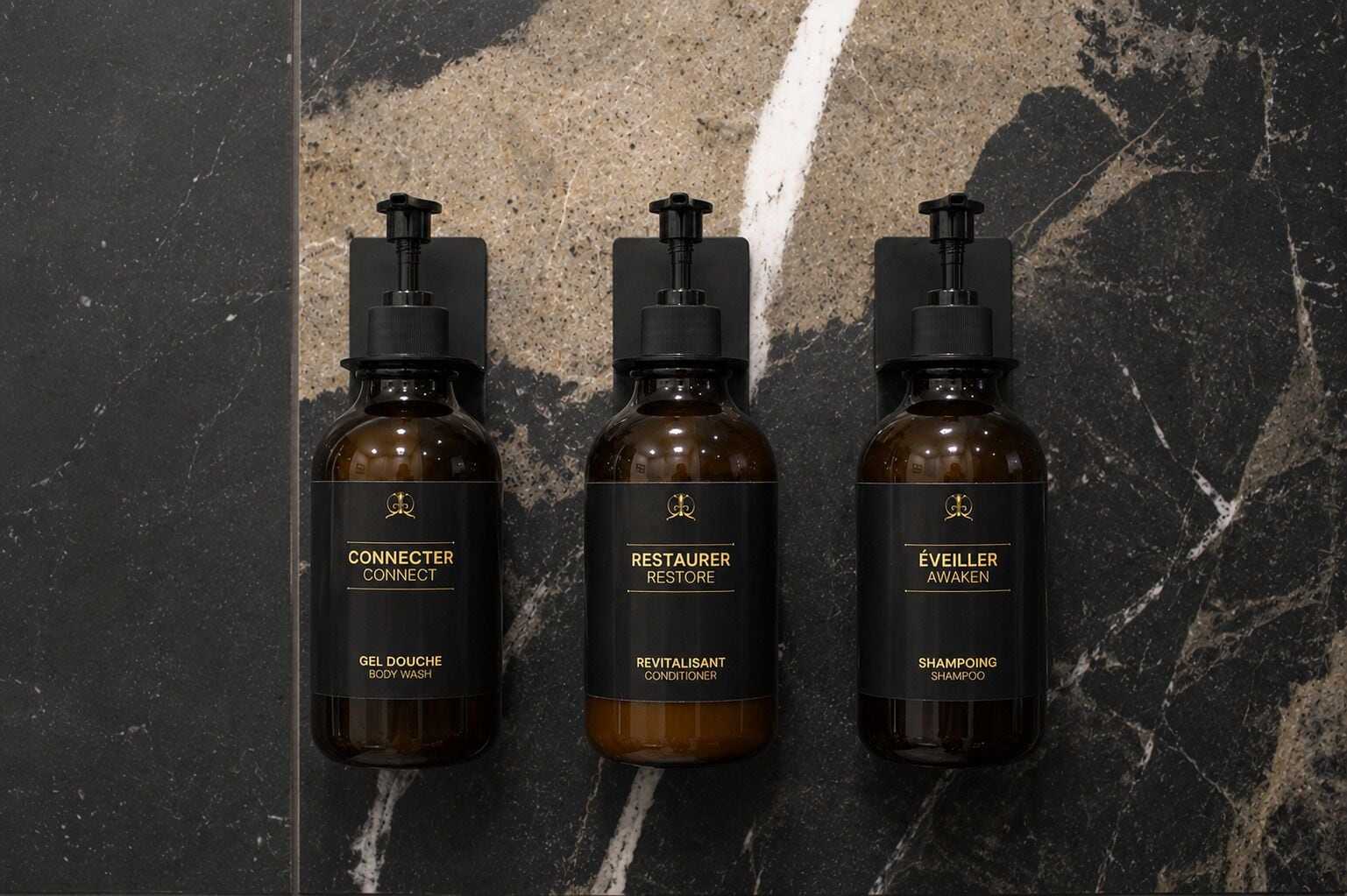 Tres botellas de gel de baño, acondicionador y champú sobre una superficie de mármol.
