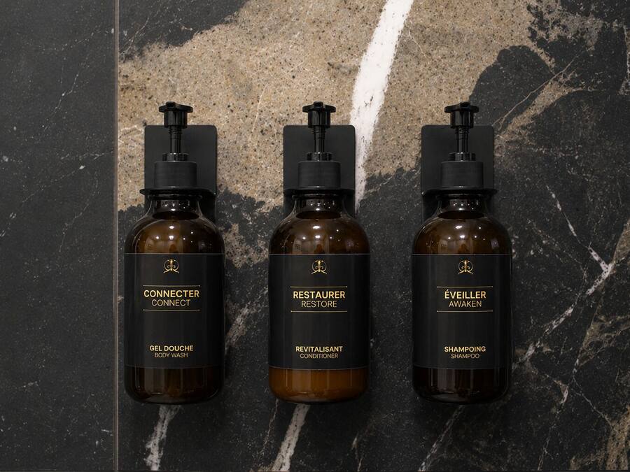 Tres botellas de gel de baño, acondicionador y champú sobre una superficie de mármol.