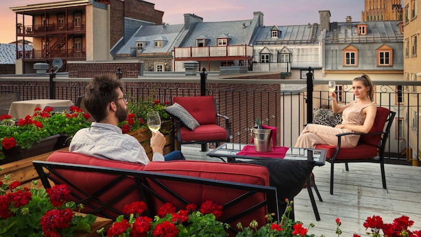 A rooftop terrace with red chairs, a table, and a view of historic buildings. - Le Manoir d'Auteuil - Par Aneyro (Québec City)