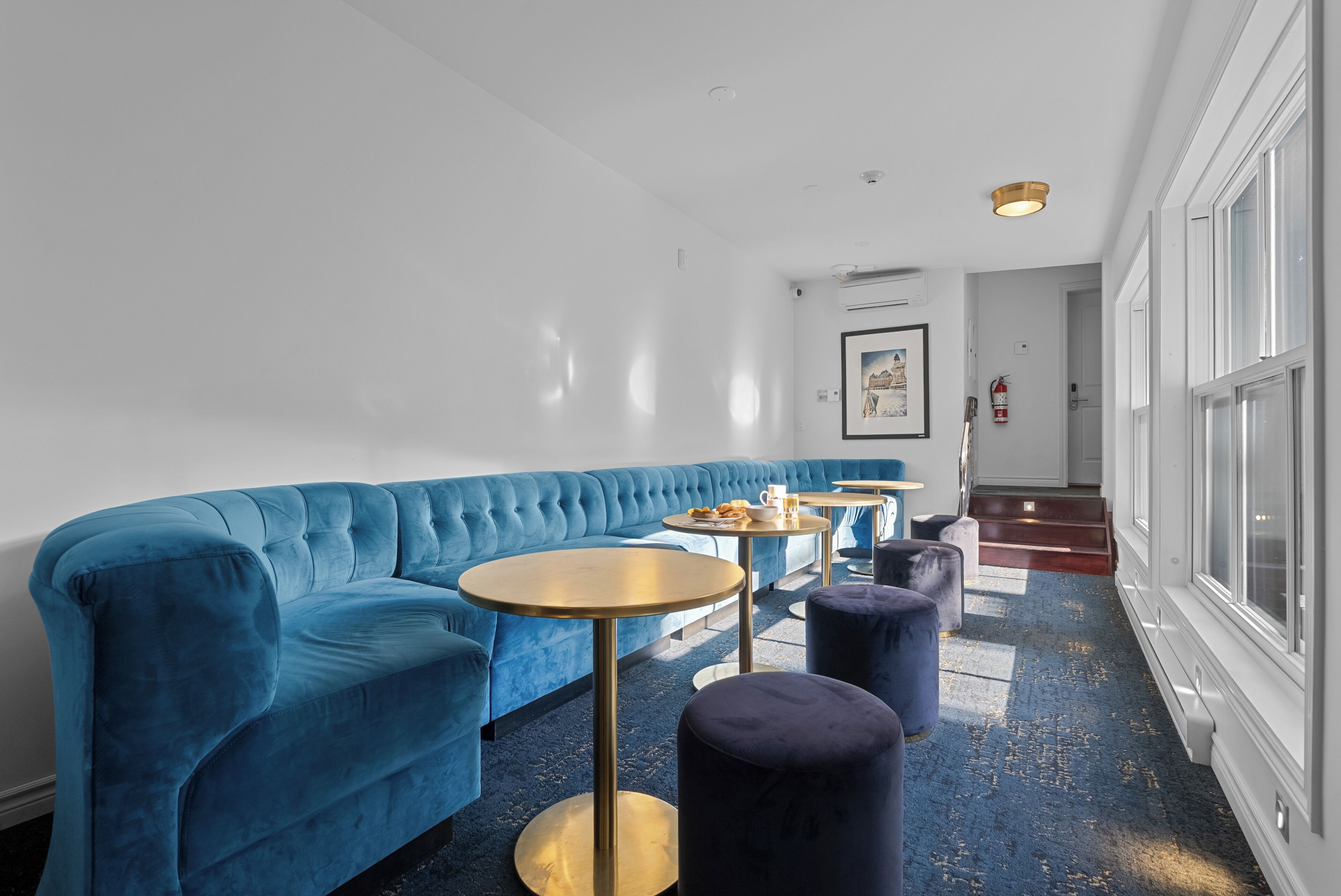 A modern lounge area with a blue sofa, round tables, and dark ottomans.