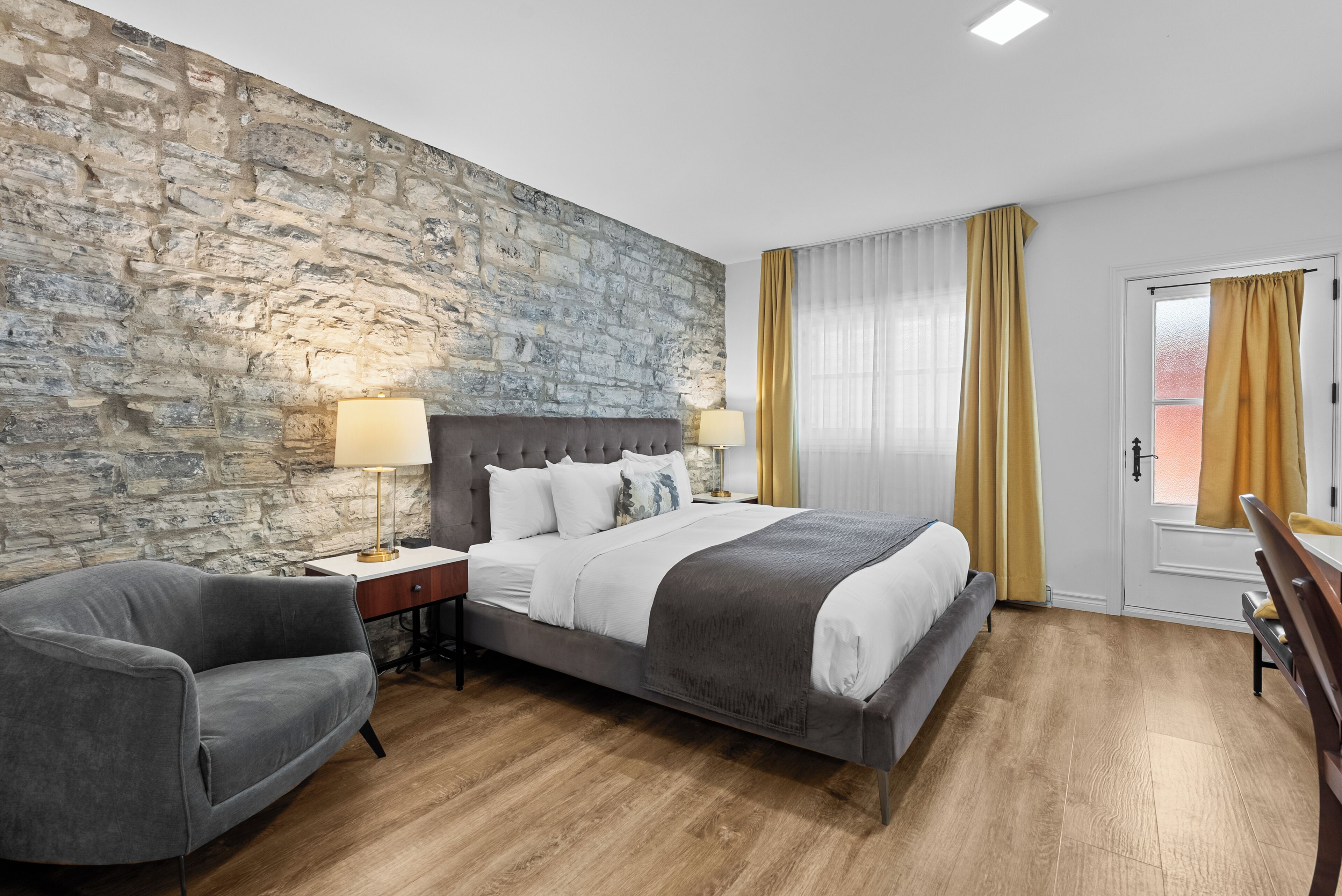 Een hotelkamer met een stenen muur, een groot bed, een bureau, een stoel en een raam met gordijnen.