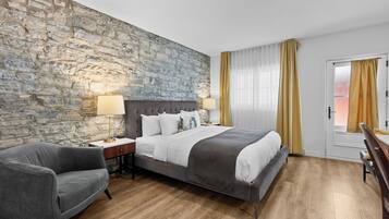 Een hotelkamer met een stenen muur, een groot bed, een bureau, een stoel en een raam met gordijnen.