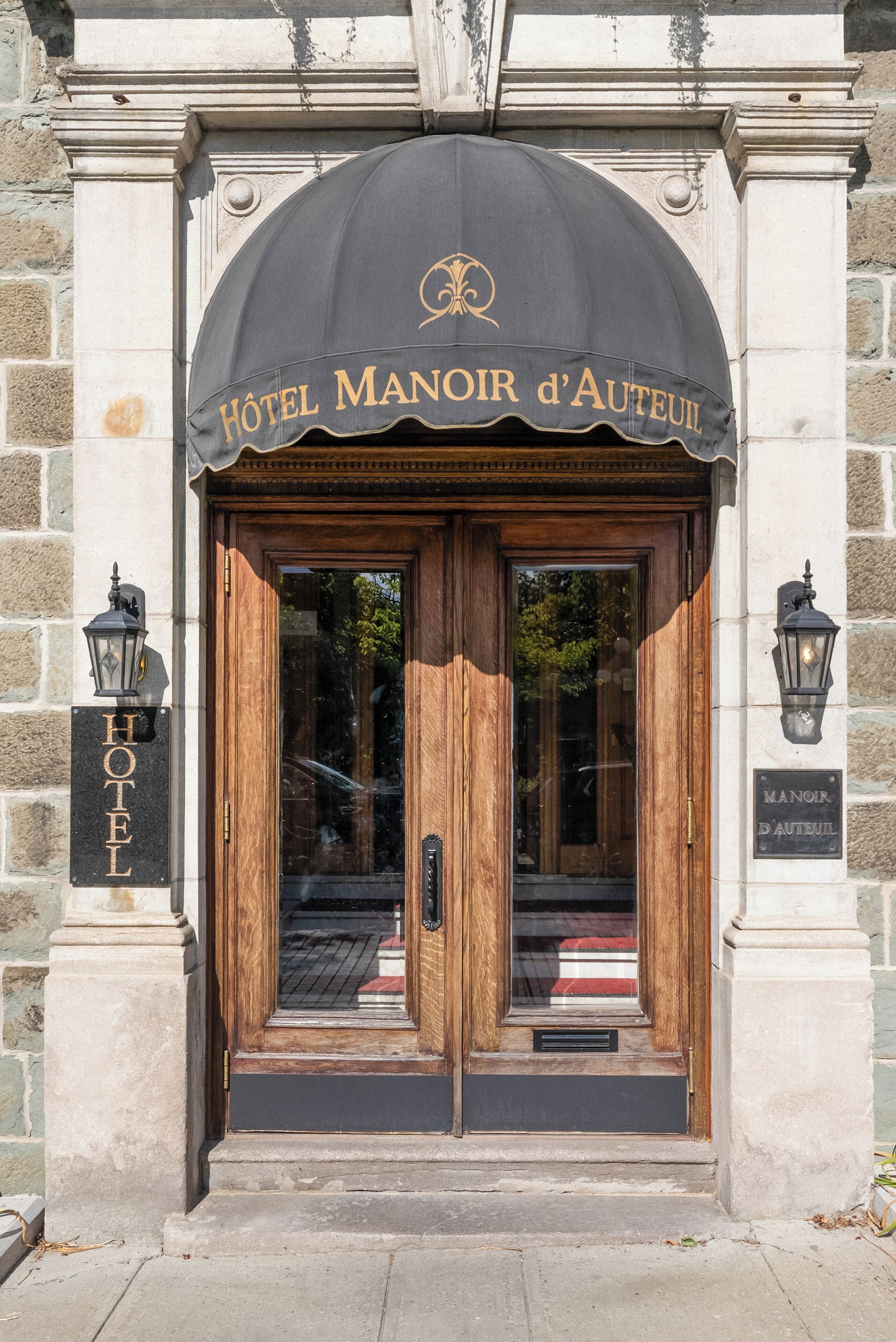 The entrance to Hotel Manoir d'Auteuil with a black awning, wooden doors, and a stone facade.