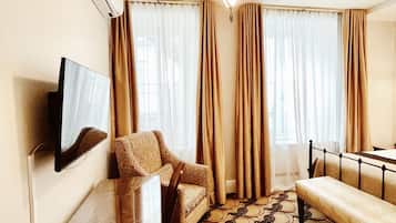 Habitación de hotel con televisión de pantalla plana, sofá, banco, alfombra estampada y una lámpara en el techo.