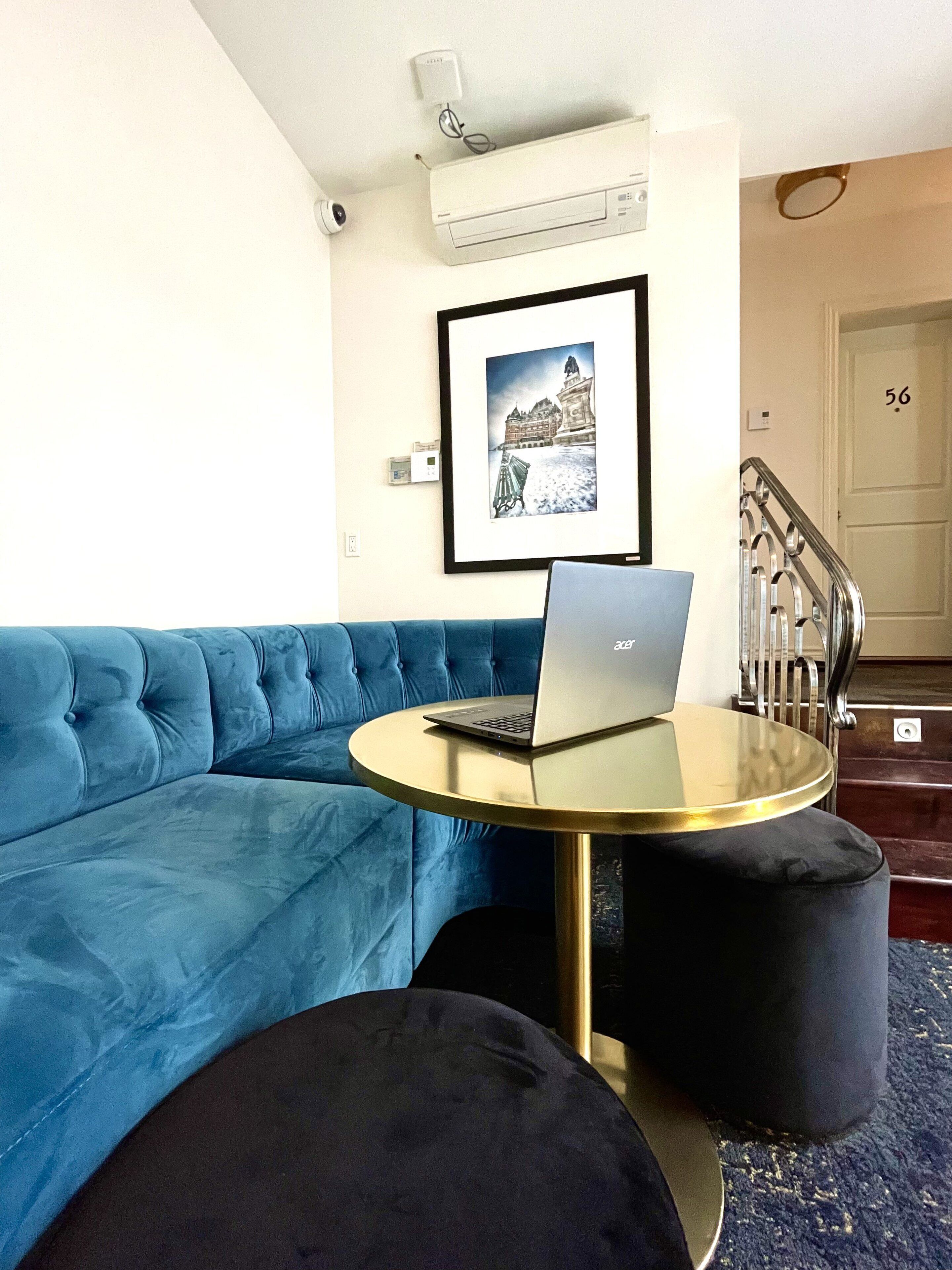 Uma sala de estar moderna com um sofá azul, uma mesa redonda com um laptop e um quadro na parede.