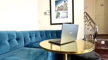 Uma sala de estar moderna com um sofá azul, uma mesa redonda com um laptop e um quadro na parede.