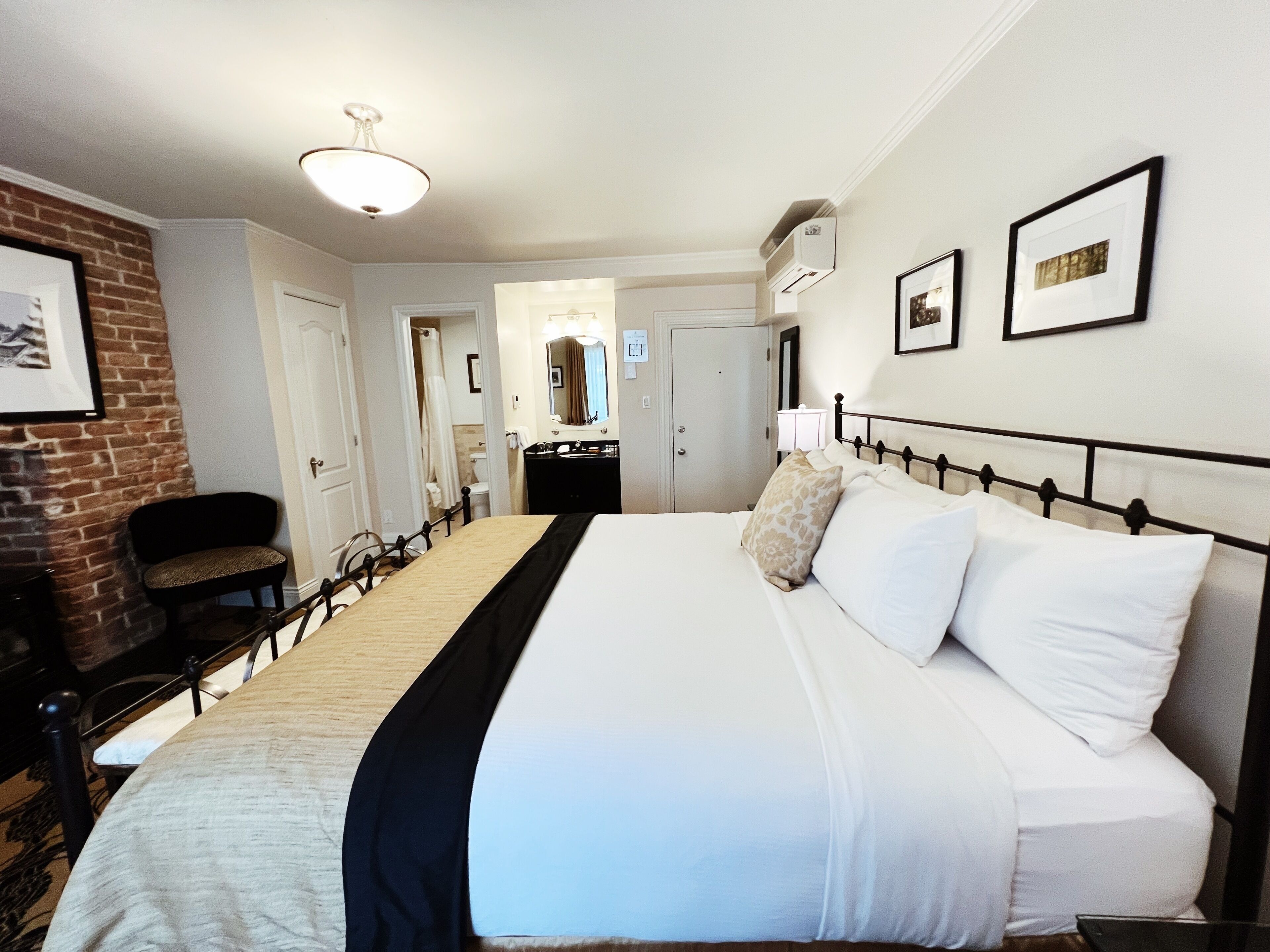 Habitación de hotel con una cama grande, una silla, un escritorio y un baño visible a través de una puerta abierta.