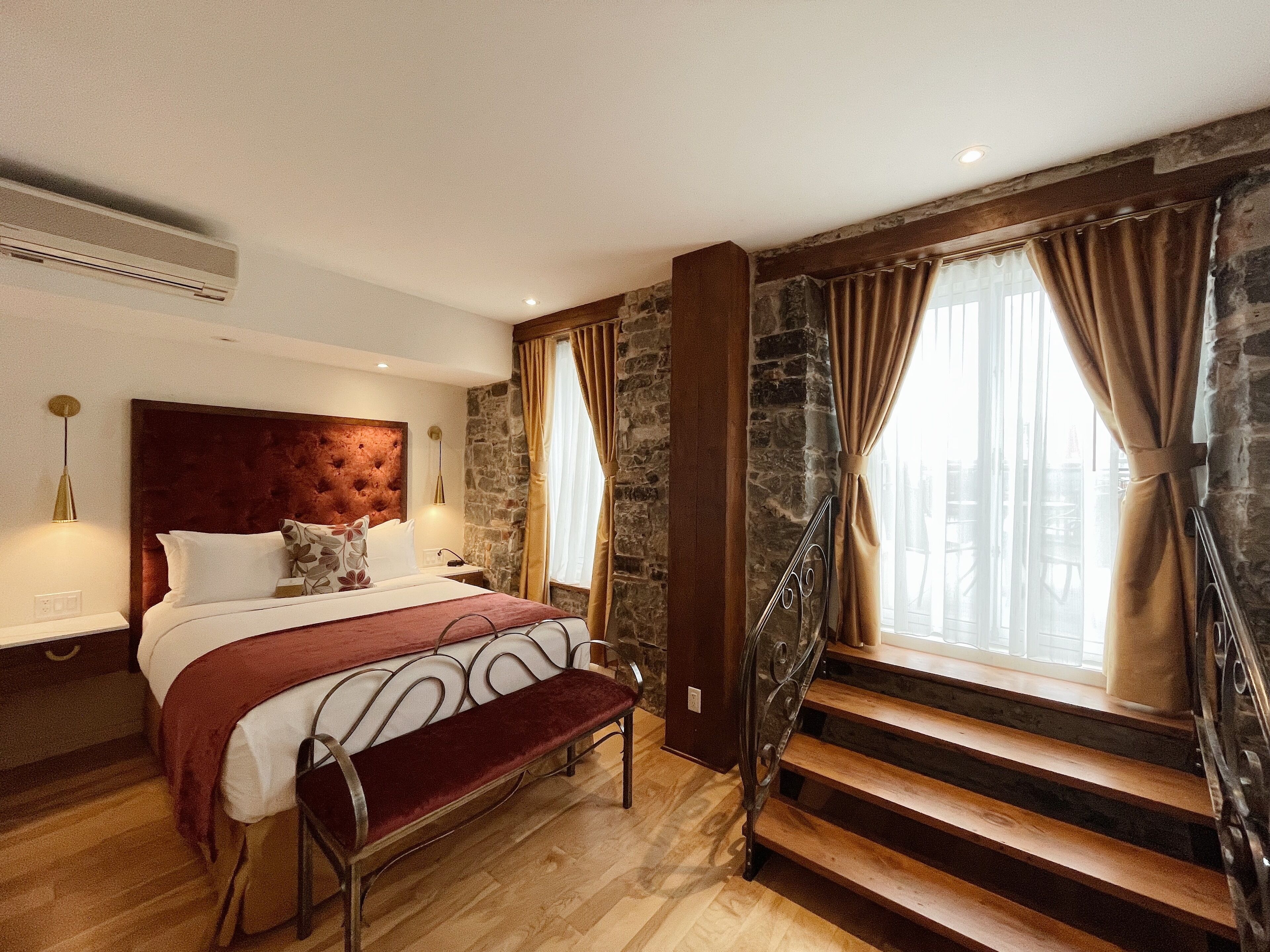 Una camera da letto con un grande letto, una panca di legno, un muro in pietra e una scala.