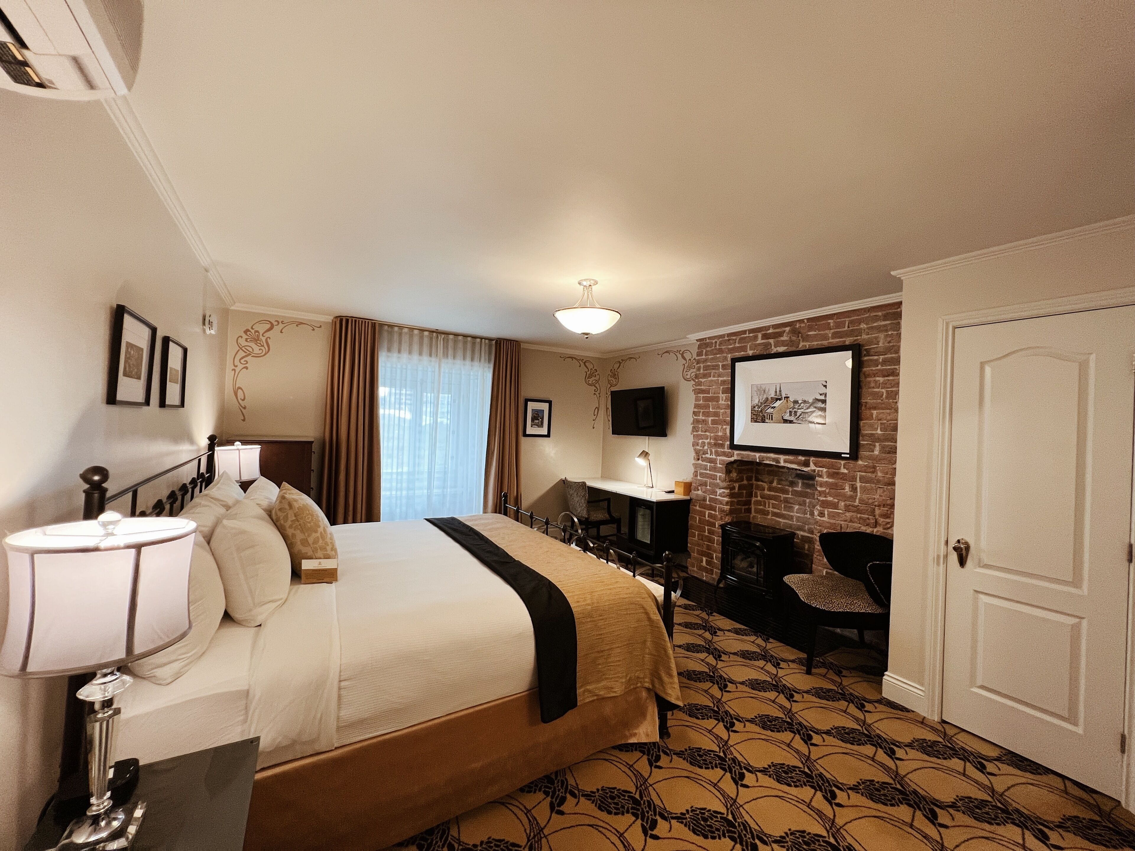 A hotel room with a large bed, a desk with a chair, a fireplace, and a TV mounted on the wall.