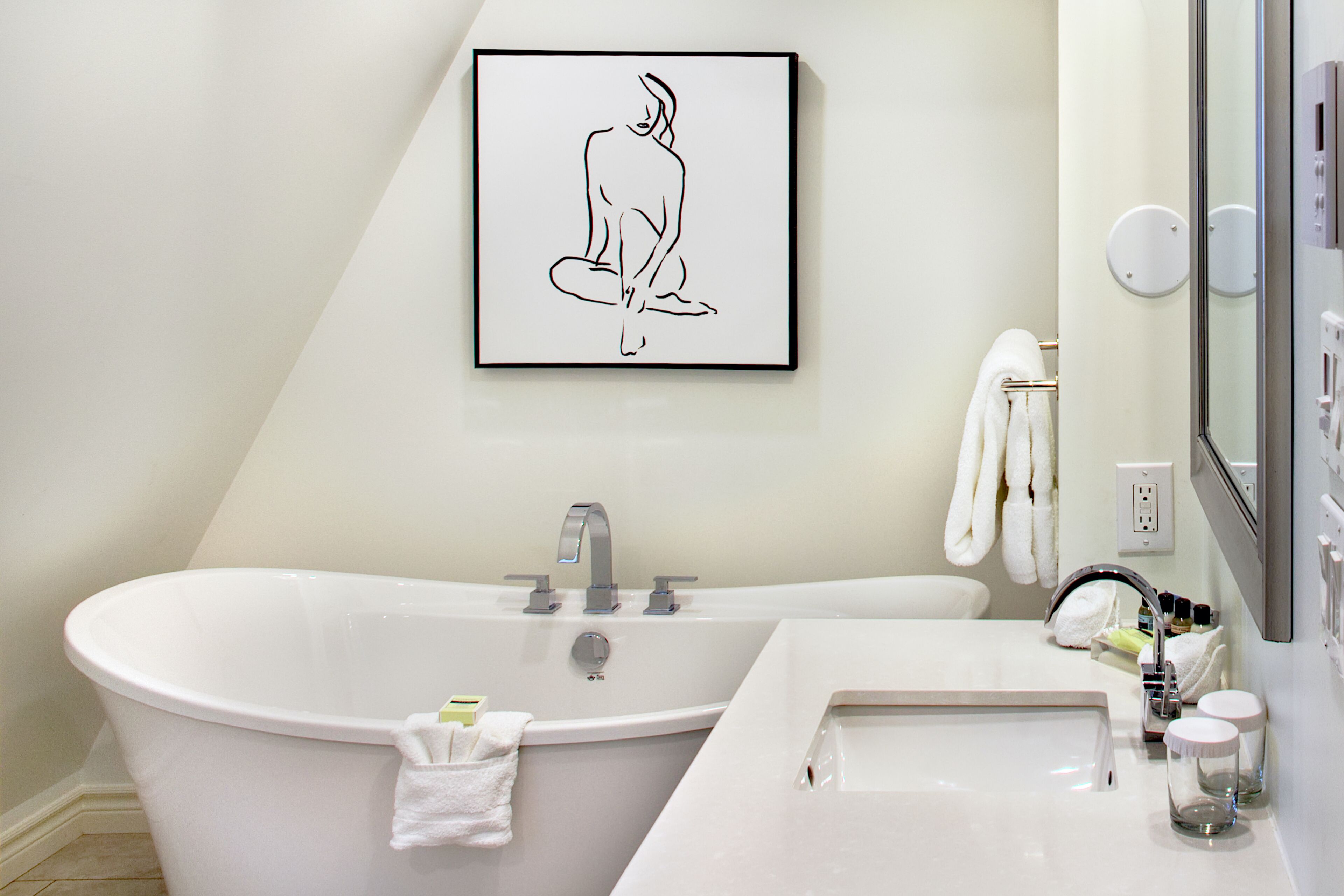 Un baño moderno con una bañera independiente, un lavamanos y una obra de arte enmarcada sobre la bañera.