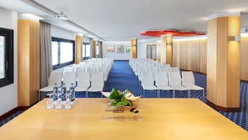 Una sala de conferencias con una larga mesa, sillas blancas y una alfombra azul.