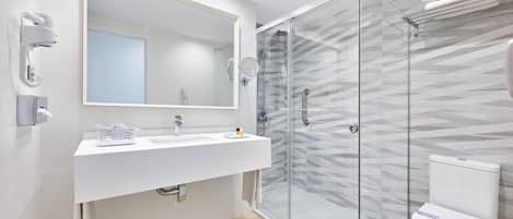 A modern bathroom with a white vanity, a large mirror, a glass-enclosed shower, and a toilet with a patterned wall.
