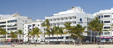 A beachfront hotel with multiple floors, palm trees, and a sandy beach.