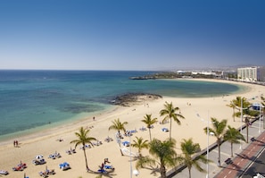 A beach with clear turquoise water, palm trees, and a promenade with beach chairs and umbrellas.