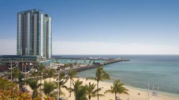 A beachside hotel with a tall building, palm trees, and a pier extending into the ocean.