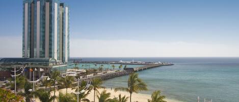 A beachside hotel with a tall building, palm trees, and a pier extending into the ocean.