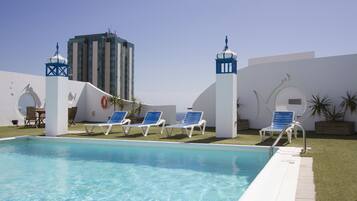 A swimming pool with lounge chairs, a tall building in the background, and a clear sky.
