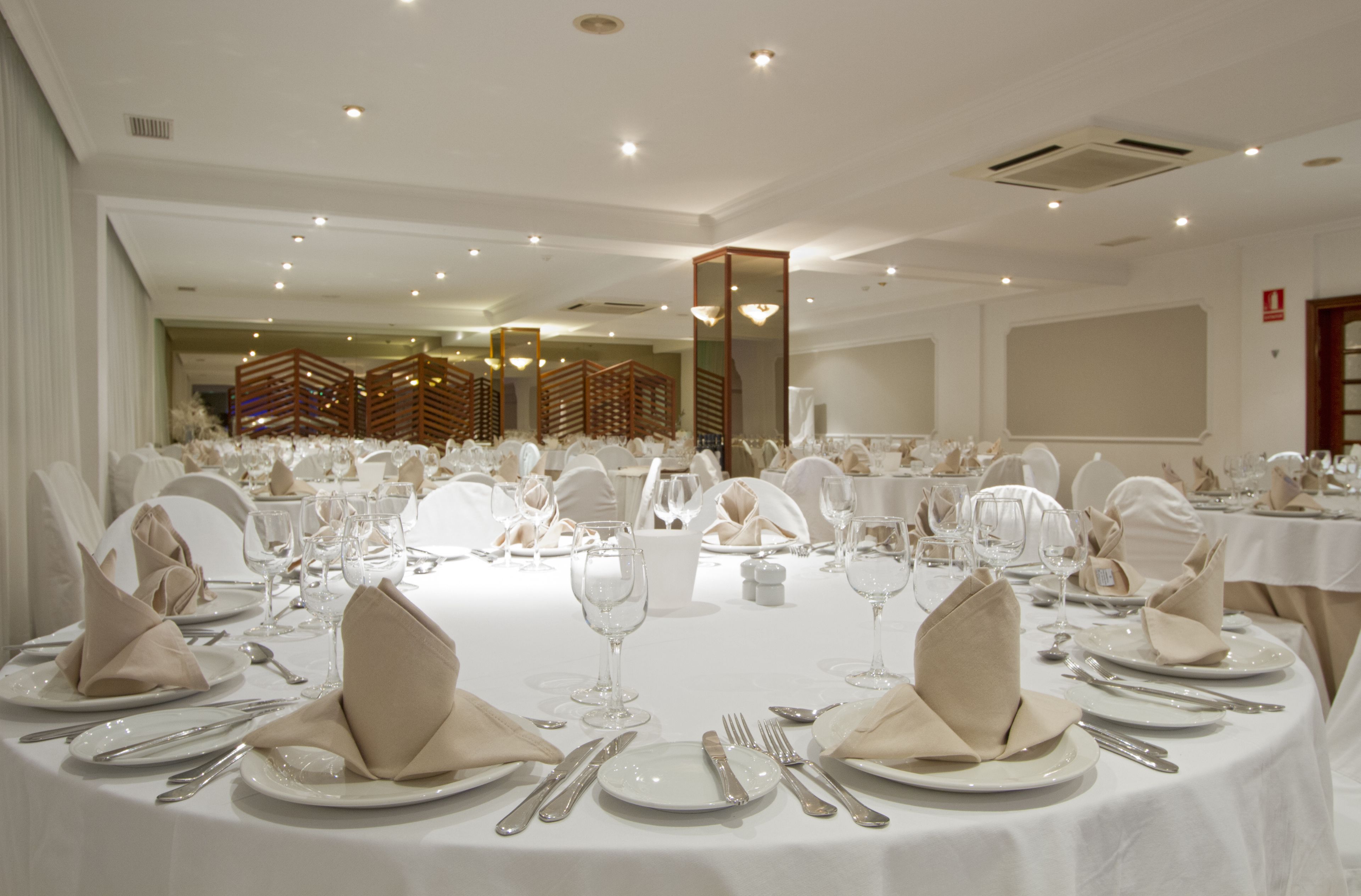 A banquet hall with round tables set for a formal event, complete with white tablecloths, folded napkins, and cutlery.