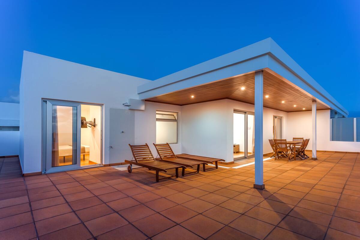Una casa moderna con un patio cubierto, que incluye un área de estar y una mesa de comedor.