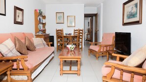 Uma sala de estar com sofá, cadeiras, mesa de centro, TV e quadros nas paredes.