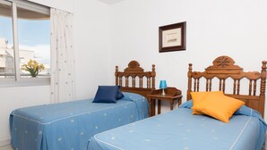 Quarto de hotel com duas camas de solteiro, cabeceira de madeira, uma mesinha com luminária e janela com vista para edifícios.