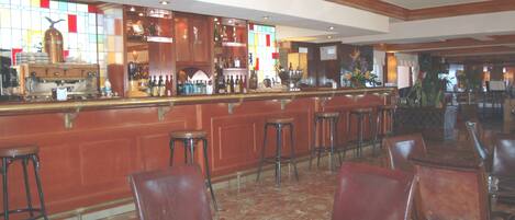 A bar area with stools and a bar counter, surrounded by leather chairs and tables.