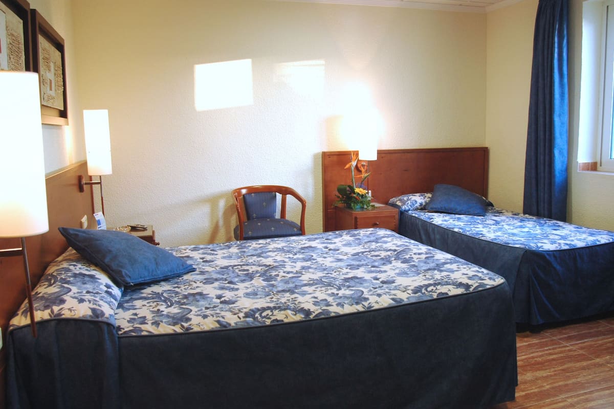 Ein Hotelzimmer mit zwei Betten, einem Sessel, einem Nachttisch und einer Lampe.