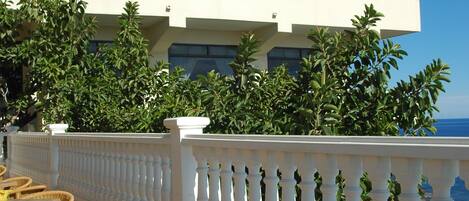 A hotel with a terrace featuring wicker furniture and a table with two glasses of beer and a plate of salad.