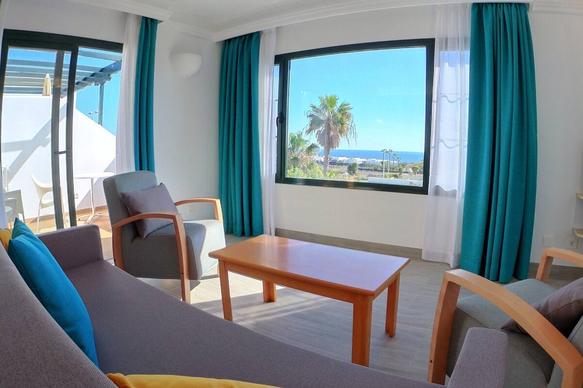 Ein modernes Hotelzimmer mit großem Fenster und Blick auf das Meer und Palmen.