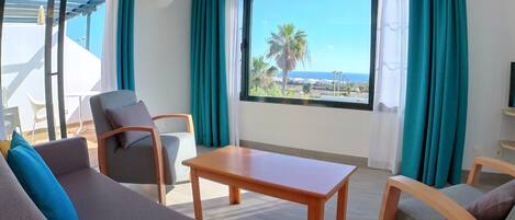 Habitación de hotel moderna con sofá, sillas, una mesa y un ventanal con vista al mar.