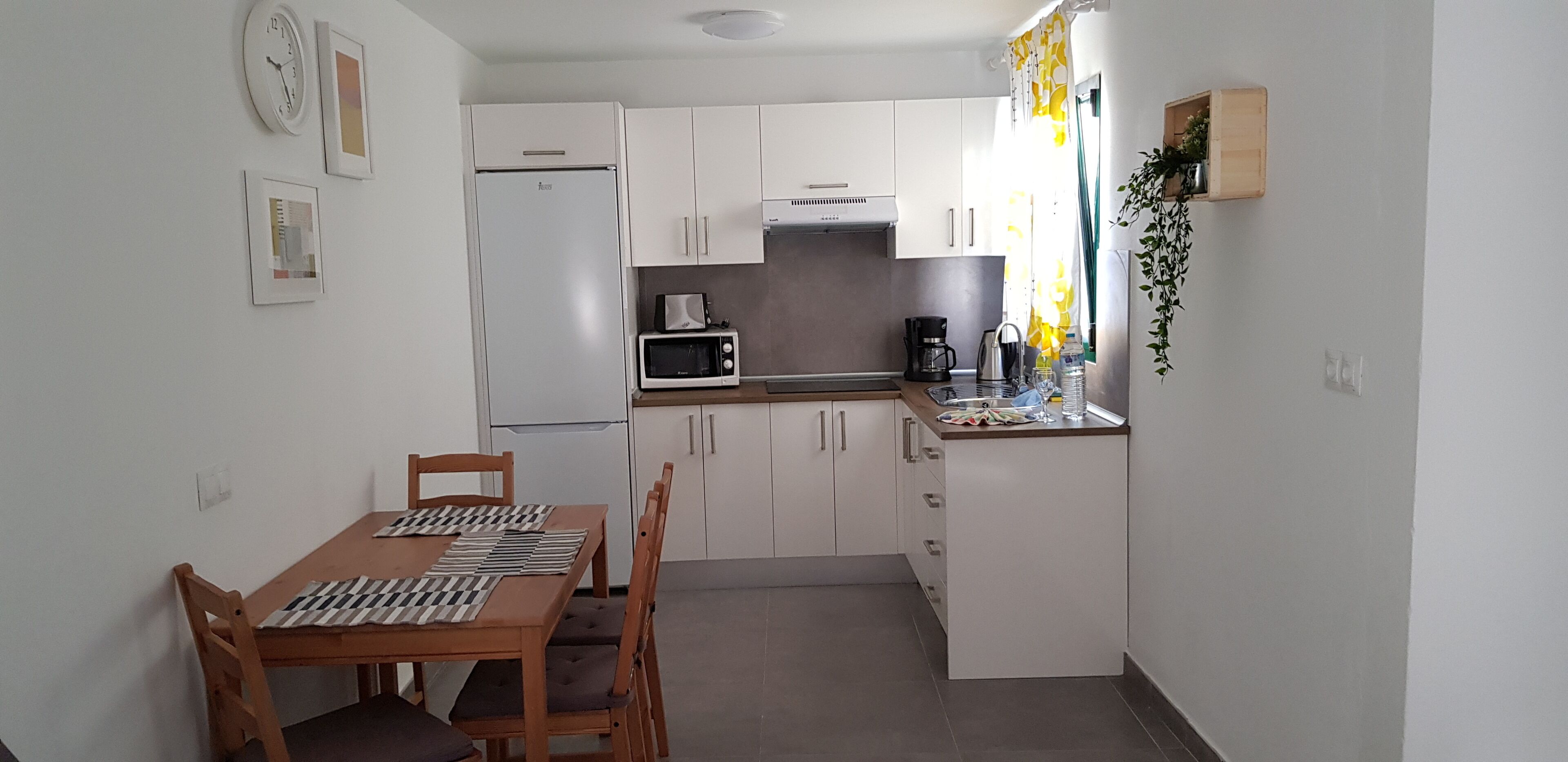 A compact kitchen with white cabinets, a microwave, a coffee maker, and a dining table with chairs.