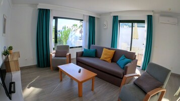 Una sala de estar moderna con sofá, sillones, una mesa de centro y un mueble para televisión.