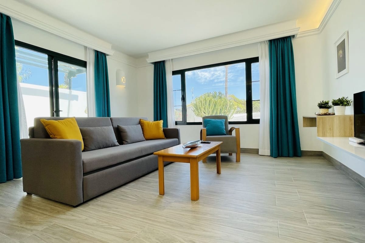 Ein modernes Wohnzimmer mit einem grauen Sofa, einem Holztisch und einem Fernseher auf einem weißen Schrank.