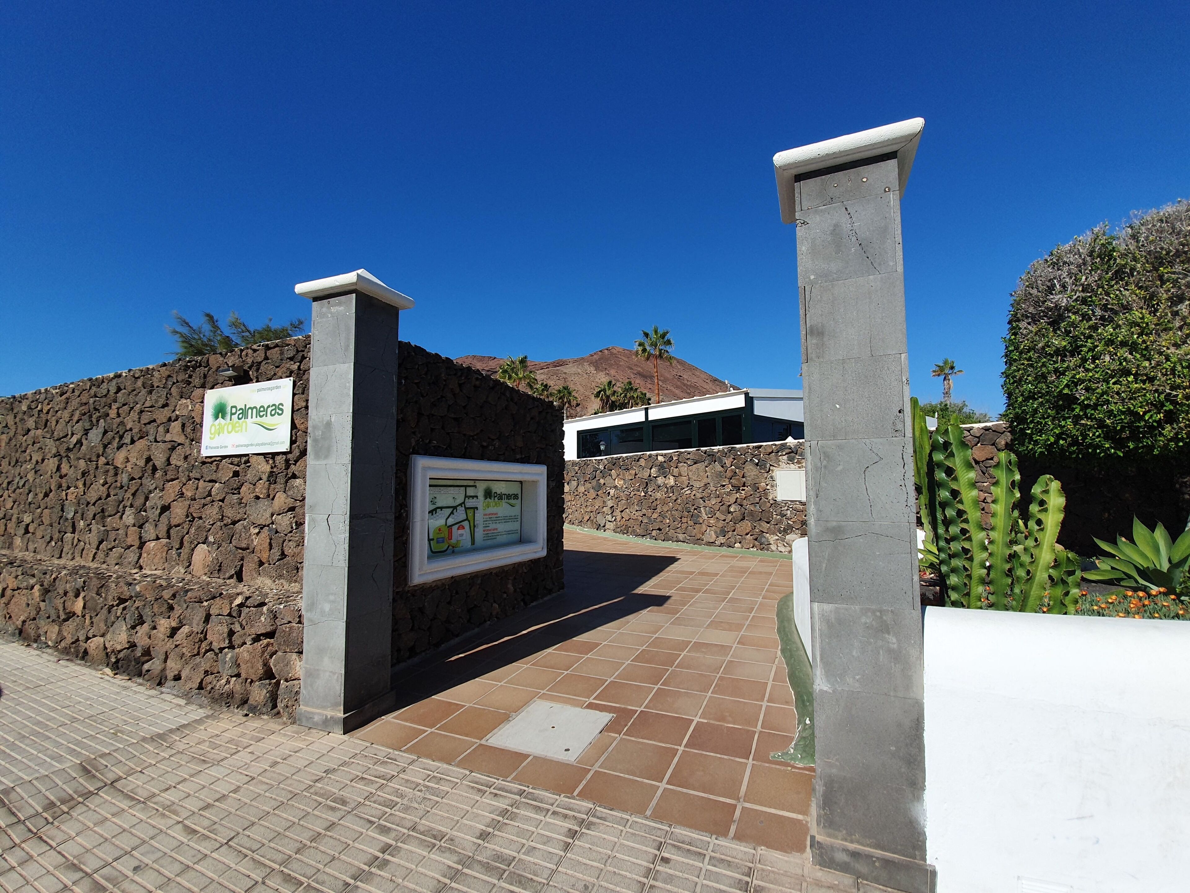 A stone wall entrance with a sign for 'Palmeras Garden'.