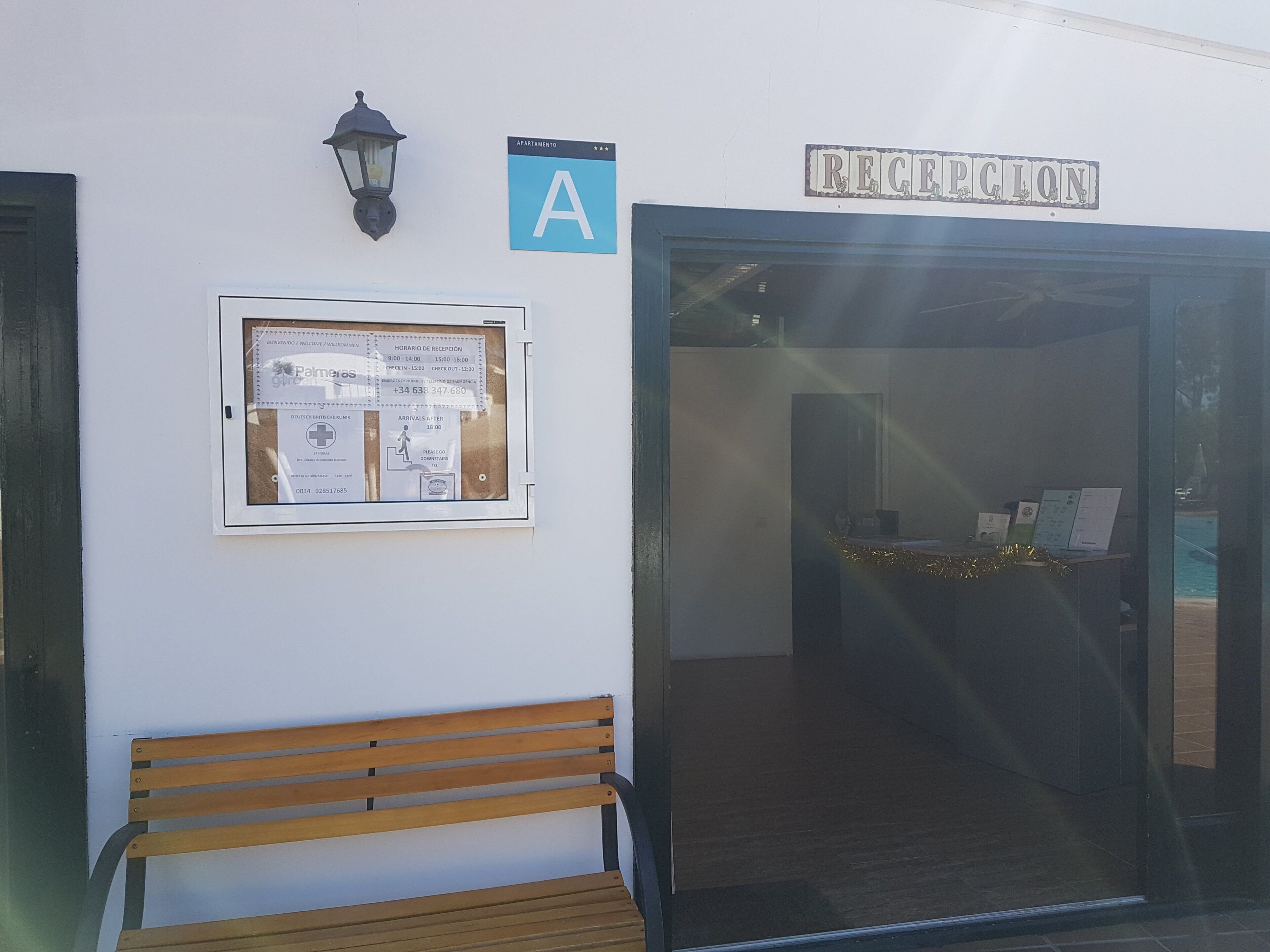 Un área de recepción con un banco, un cartel que indica 'Reception' y un letrero azul en forma de 'A' sobre un tablón de anuncios.
