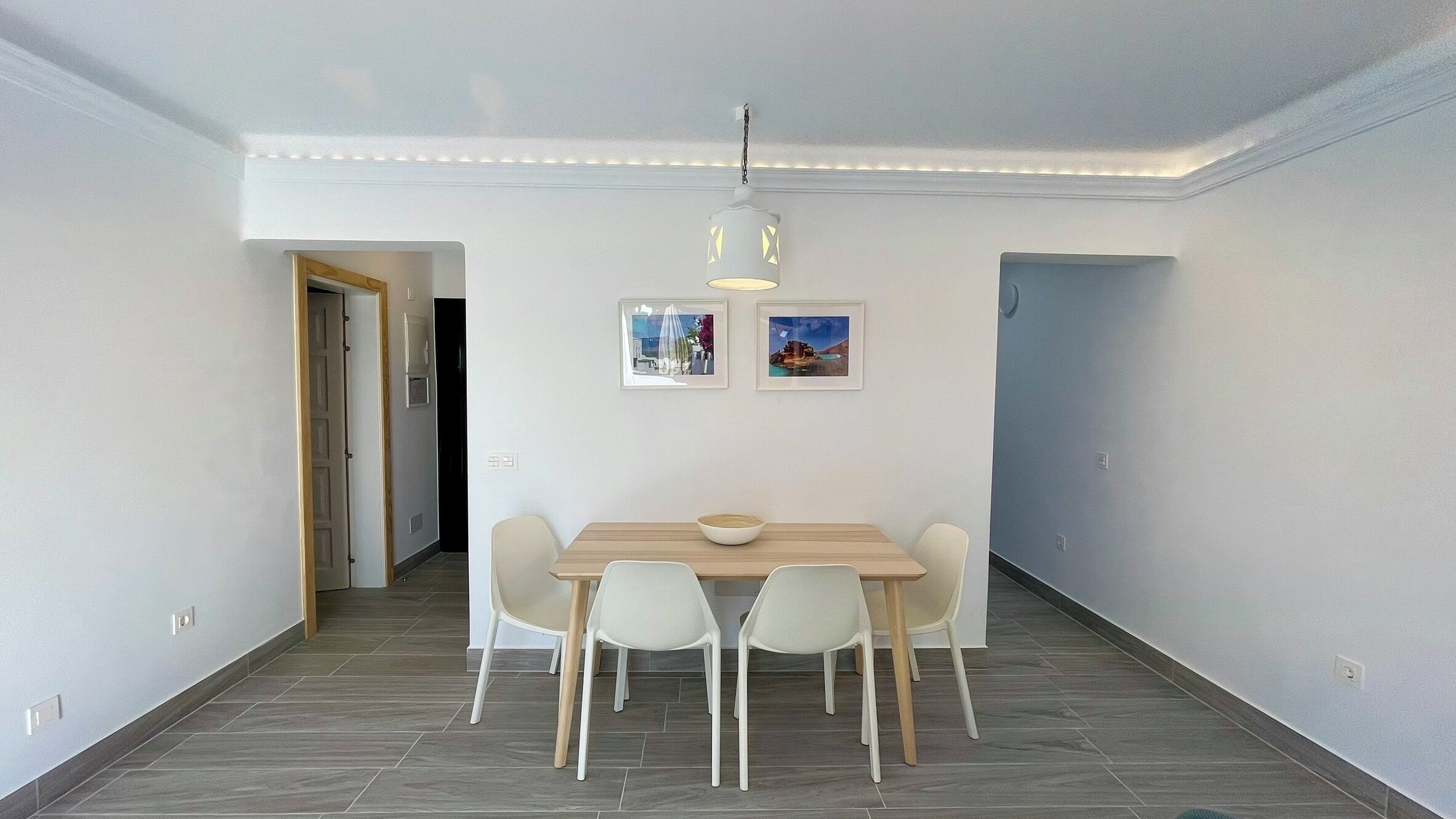 Zona pranzo con tavolo e sedie, una lampada a sospensione e due quadri appesi al muro.