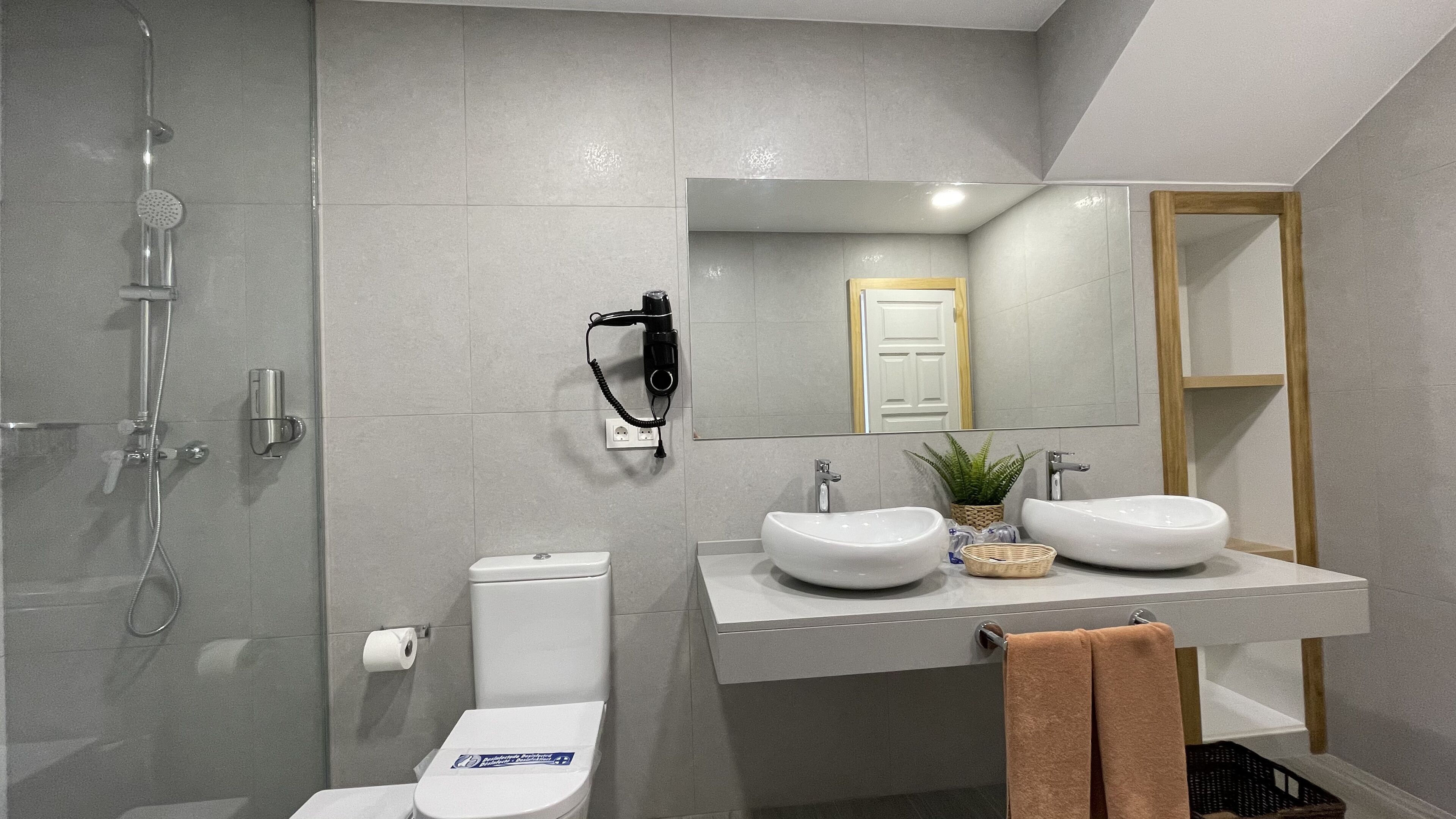 Un bagno moderno con doccia, WC e due lavandini.