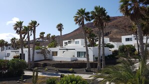 A modern resort with white buildings, palm trees, and a mountain in the background. - Palmeras Garden (Yaiza)