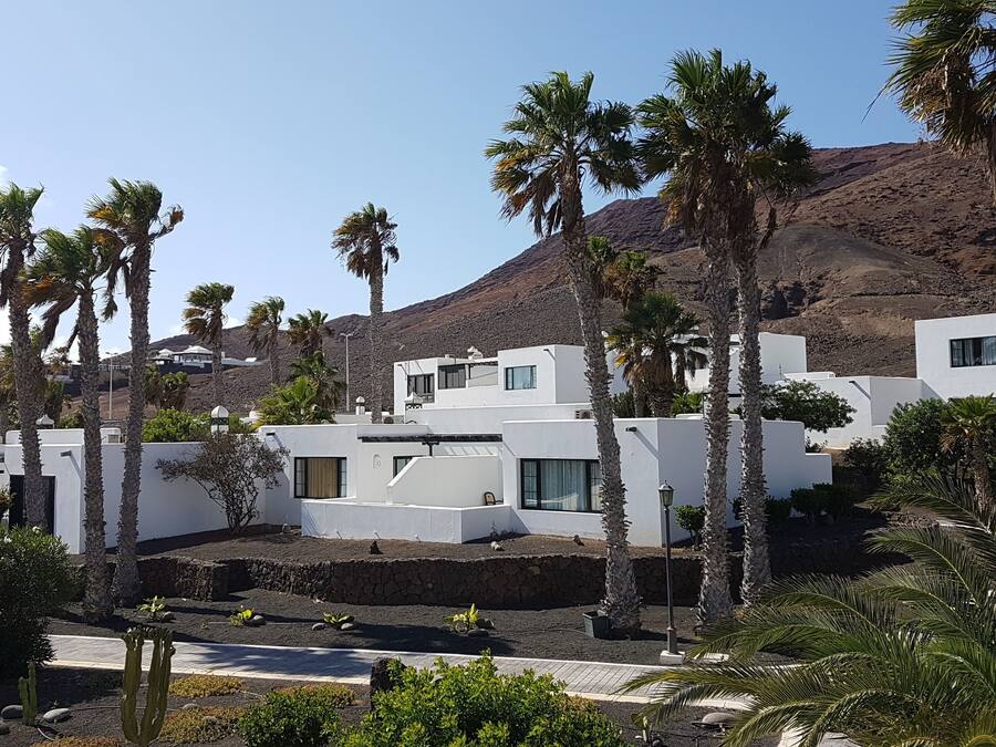 A modern resort with white buildings, palm trees, and a mountain in the background.