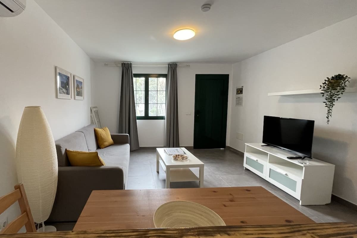 Ein Wohnzimmer mit einer Couch, einem Couchtisch, einem Fernseher auf einem Schrank und einem Esstisch mit Stühlen.